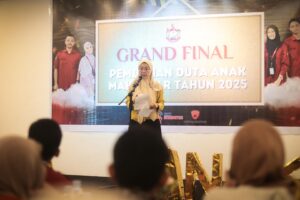 Melinda Aksa memberikan sambutan di atas panggung pada acara Grand Final Pemilihan Duta Anak Makassar 2025, dengan latar belakang spanduk acara dan audiens yang menyimak di depan panggung.