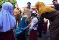 Ketua TP PKK Kota Makassar, Melinda Aksa, didampingi Wali Kota Munafri Arifuddin, memasangkan atribut seragam kepada salah satu siswa baru dalam penyaluran perdana seragam sekolah gratis di SD Lariang Bangi I, Senin (21/7/2025).