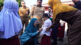 Ketua TP PKK Kota Makassar, Melinda Aksa, didampingi Wali Kota Munafri Arifuddin, memasangkan atribut seragam kepada salah satu siswa baru dalam penyaluran perdana seragam sekolah gratis di SD Lariang Bangi I, Senin (21/7/2025).