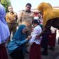 Ketua TP PKK Kota Makassar, Melinda Aksa, didampingi Wali Kota Munafri Arifuddin, memasangkan atribut seragam kepada salah satu siswa baru dalam penyaluran perdana seragam sekolah gratis di SD Lariang Bangi I, Senin (21/7/2025).